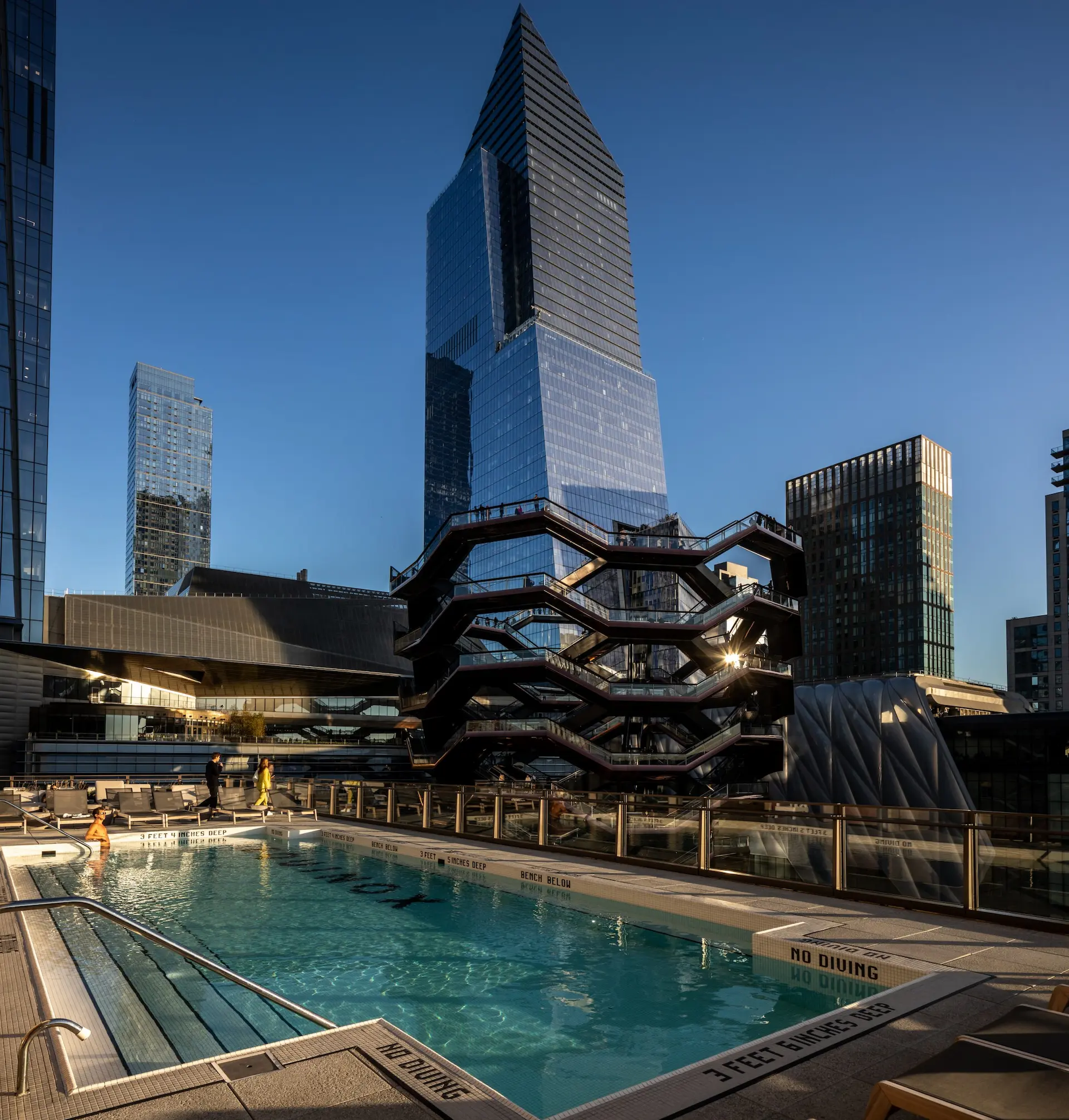 man in outdoor pool overlooking hudson yards plaza and vessel with view of skyscrapers
