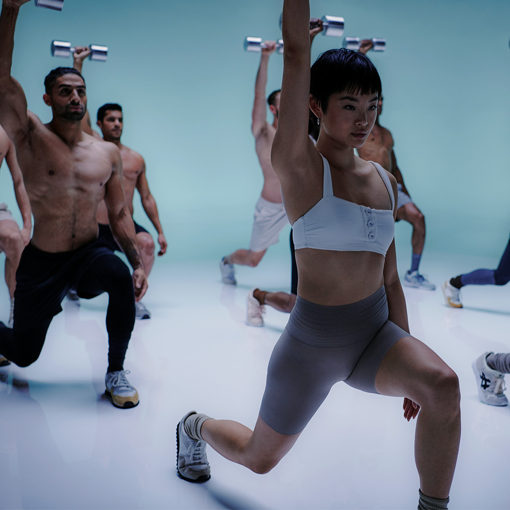 Group of individuals participating in a weight training workout, led by a fitness instructor in a well-lit, modern gym environment.